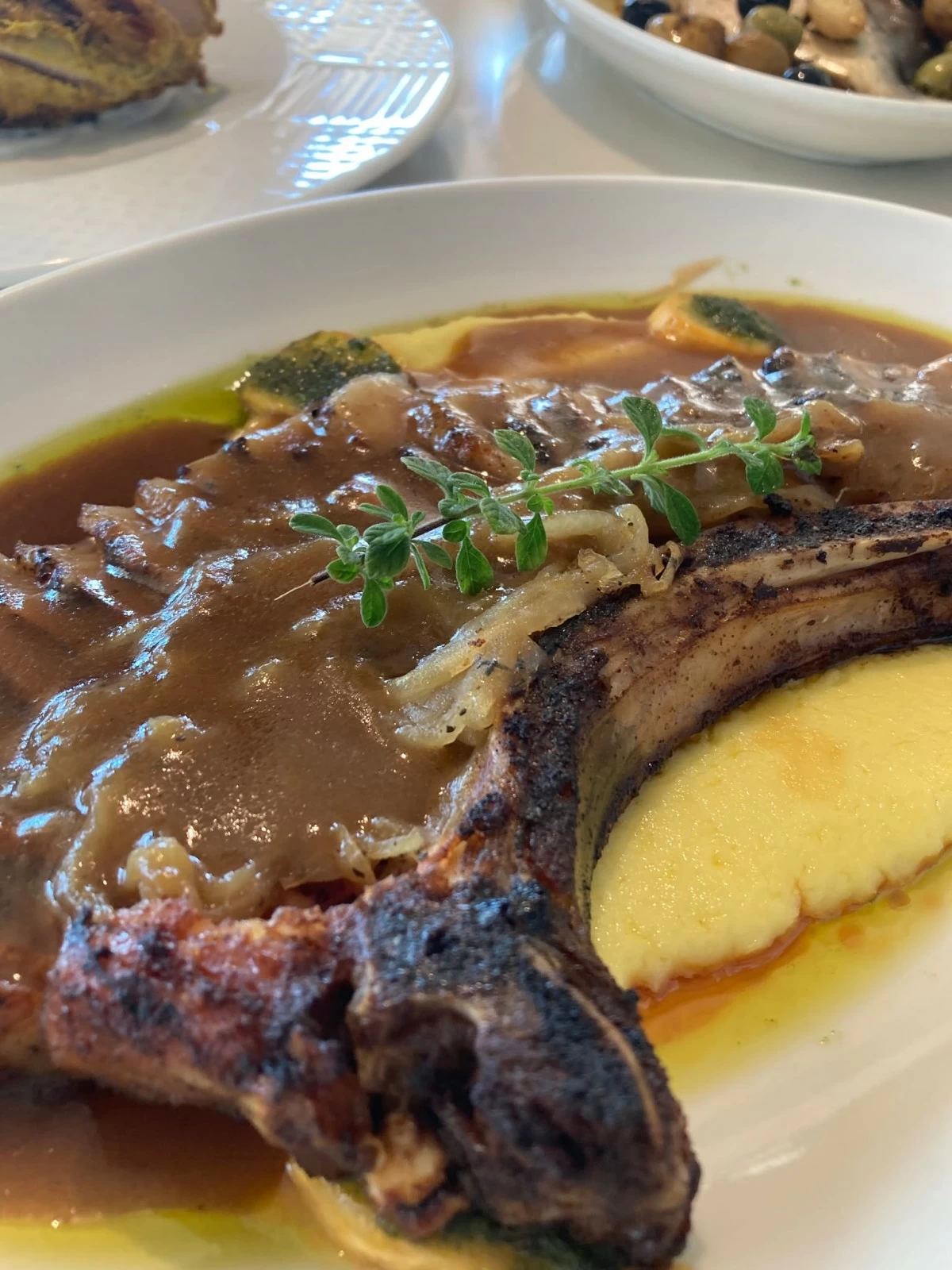 MEAL FIT FOR ROYALTY Taza Fresh Table's Tomahawk Pork Chop served with caramelized onions and bananas, salsa verde, and pork jus