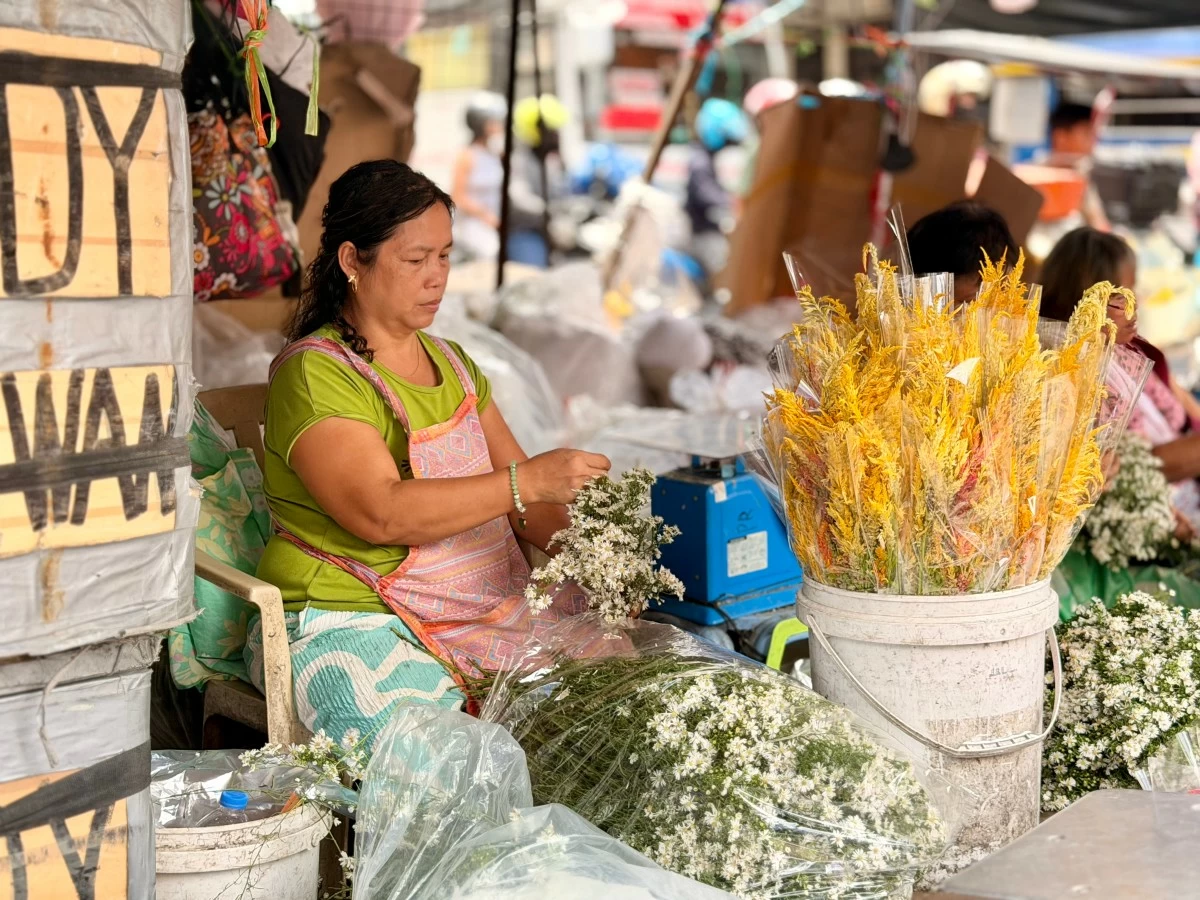 A woman in an apron weighs and sorts flower stems at a stall along Dos Castillas Street in Dangwa, carefully preparing bundles for Mother’s Day buyers.