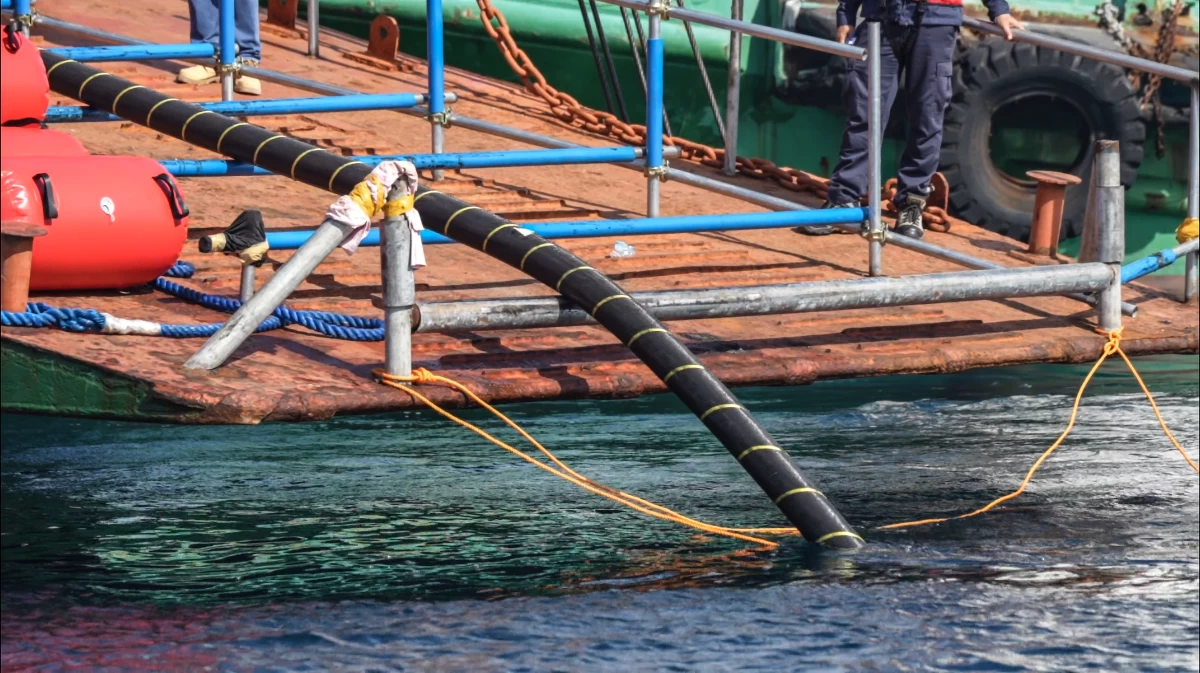 As the main vessel traverses the Pakiputan Strait, the submarine cable is deployed, rolling steadily into the depths.