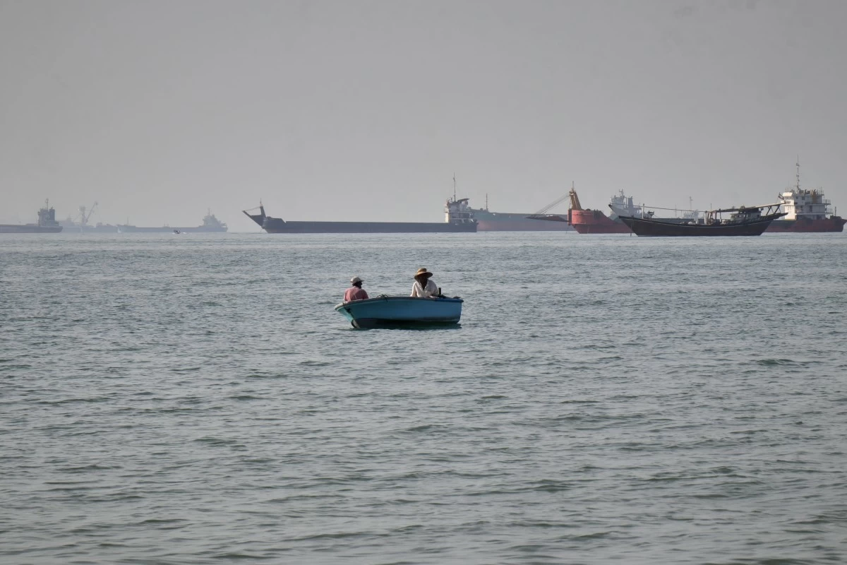 Two men sit in a small boat on the water as a mix of bulk carriers, cargo ships, and service vessels line the horizon in the Strait of Hormuz off Bandar Abbas, Iran, Monday, April 27, 2026.(Razieh Poudat/ISNA via AP)