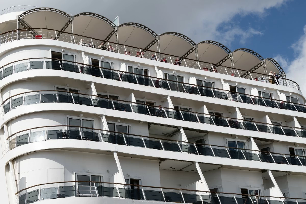 Passengers stand aboard the British cruise ship Ambition, as French authorities have ordered 1,700 passengers and crew to stay on board due to a gastrointestinal illness outbreak, in Bordeaux, southwestern France, Wednesday, May 13, 2026. (AP Photo/Caroline Blumberg)