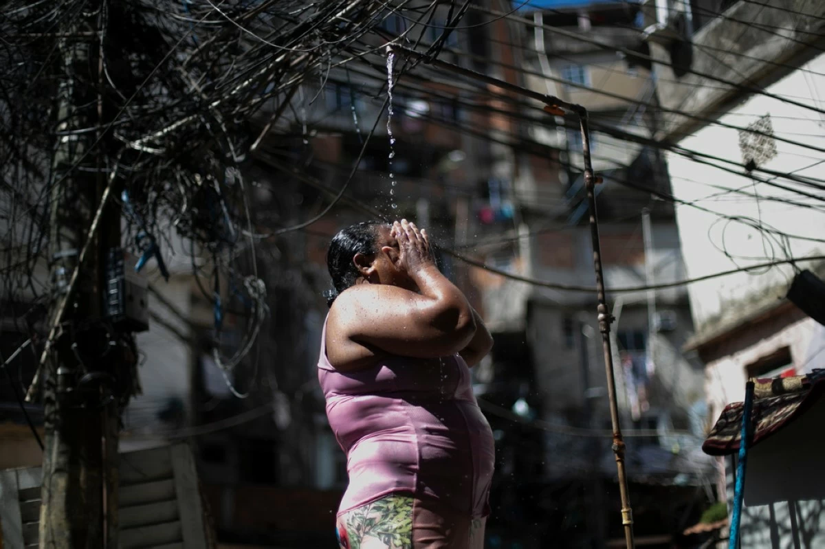 Kelly Cristina da Cruz cools off in a public shower in the Rocinha favela amid a heat wave in Rio de Janeiro, Jan. 15, 2026. (AP Photo/Bruna Prado)
