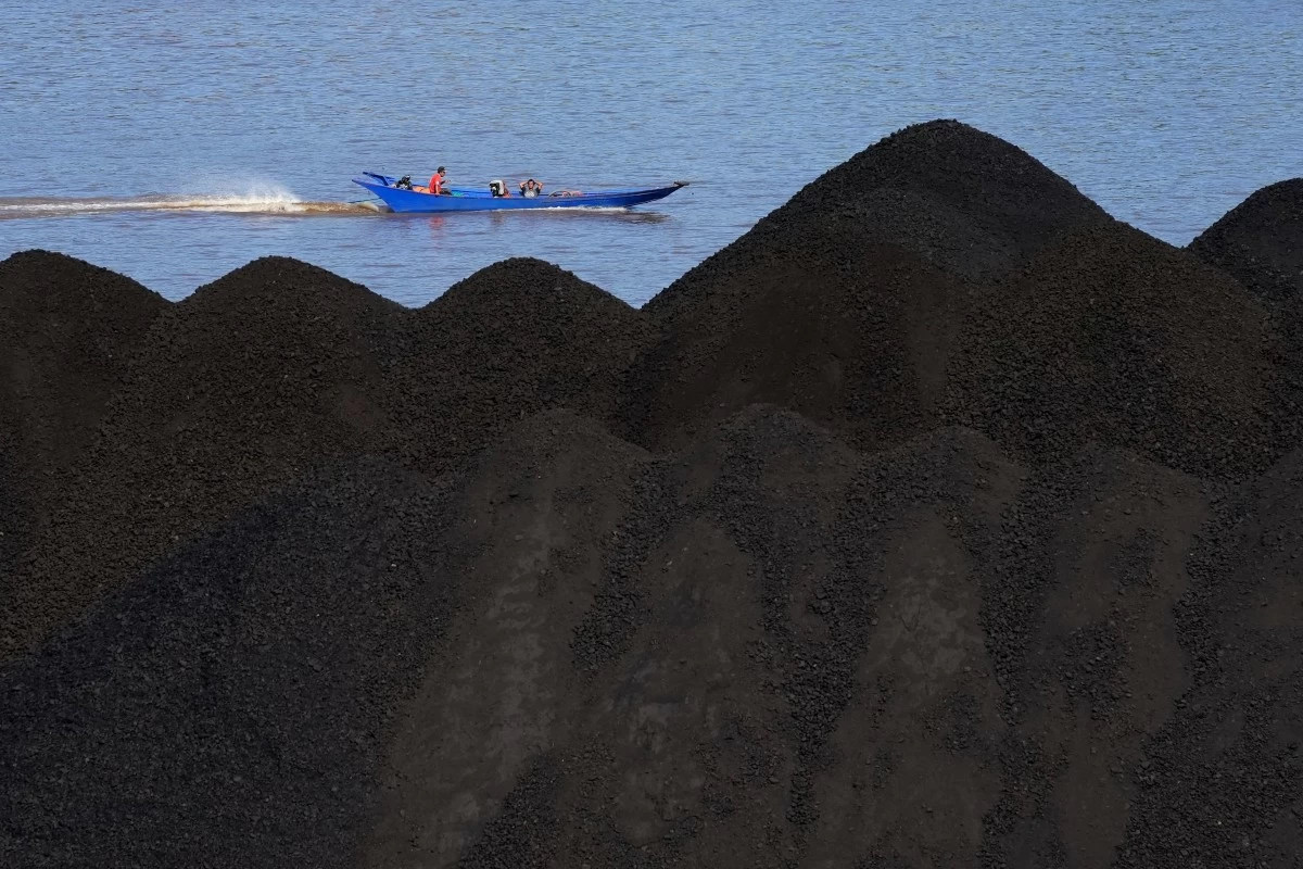 FILE - A boat cruises past a coal piled up on a barge on Mahakam River in Samarinda, East Kalimantan, Indonesia, Dec. 19, 2022. (AP Photo/Dita Alangkara, File)