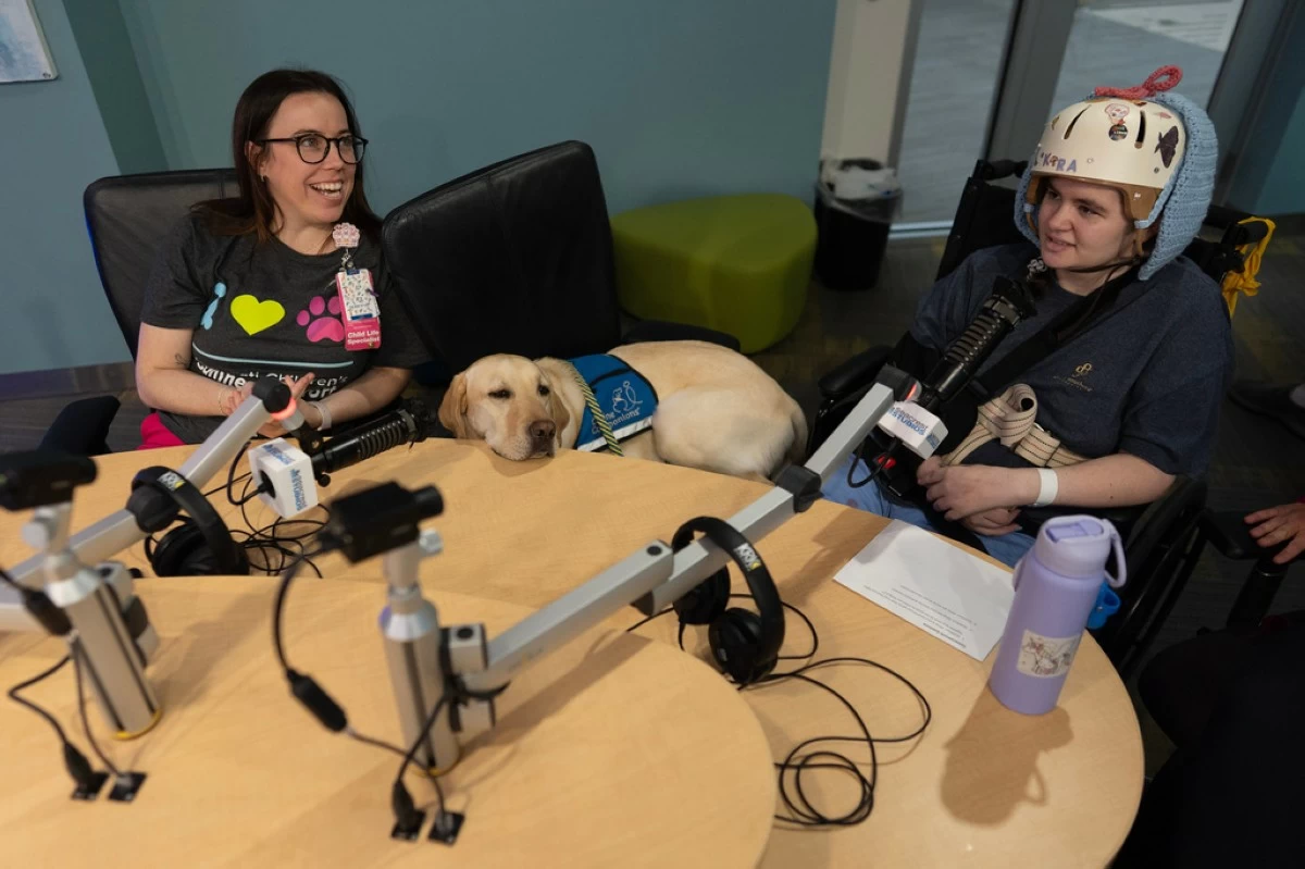 Cincinnati Children's Hospital Child Life Specialist Maggie O'Grady, left, and facility dog Grover, center, work with patient Kira Hodge at the hospital's Seacrest Studios to produce a closed-circuit television show beamed into patient rooms, at Cincinnati Children's Hospital in Cincinnati, Monday, May 4, 2026. (AP Photo/Carolyn Kaster)