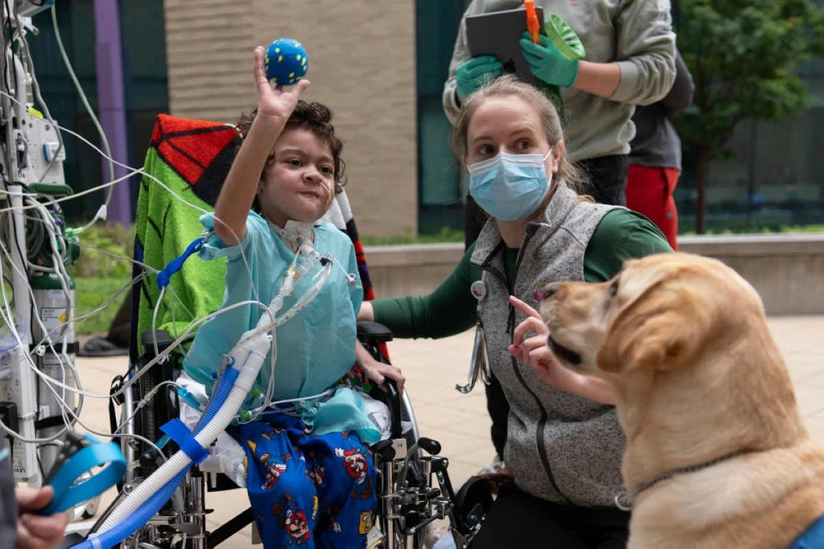 Five-year-old patient Calvin Owens throws a ball for facility dog Hadley with physical therapist Paige Torbet, right, during a physical therapy visit on the patio of Cincinnati Children's Hospital in Cincinnati, Monday, May 4, 2026. (AP Photo/Carolyn Kaster)