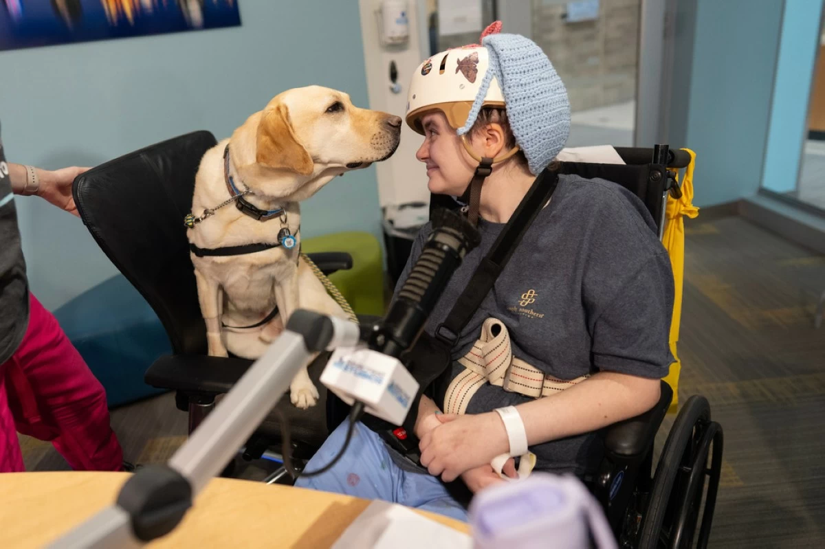 Cincinnati Children's Hospital facility dog Grover, left, looks to patient Kira Hodge at the hospital's Seacrest Studios as they produce a closed-circuit television show beamed into patient rooms, at Cincinnati Children's Hospital in Cincinnati, Monday, May 4, 2026. (AP Photo/Carolyn Kaster)