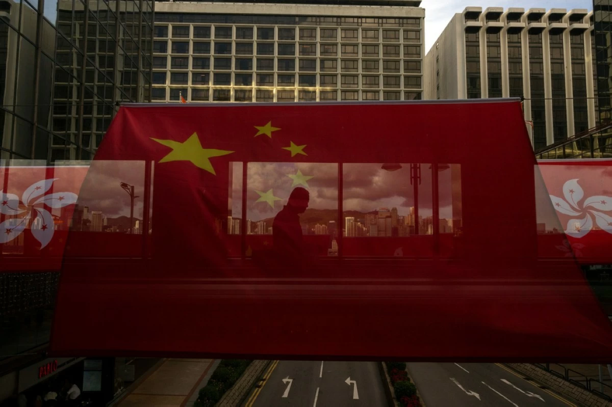 A pedestrian walks through a footbridge is silhouetted as Chinese and Hong Kong flags are strung to mark the 26th anniversary of the city's handover from Britain to China in Hong Kong, on June 27, 2023. (AP Photo/Louise Delmotte, File)