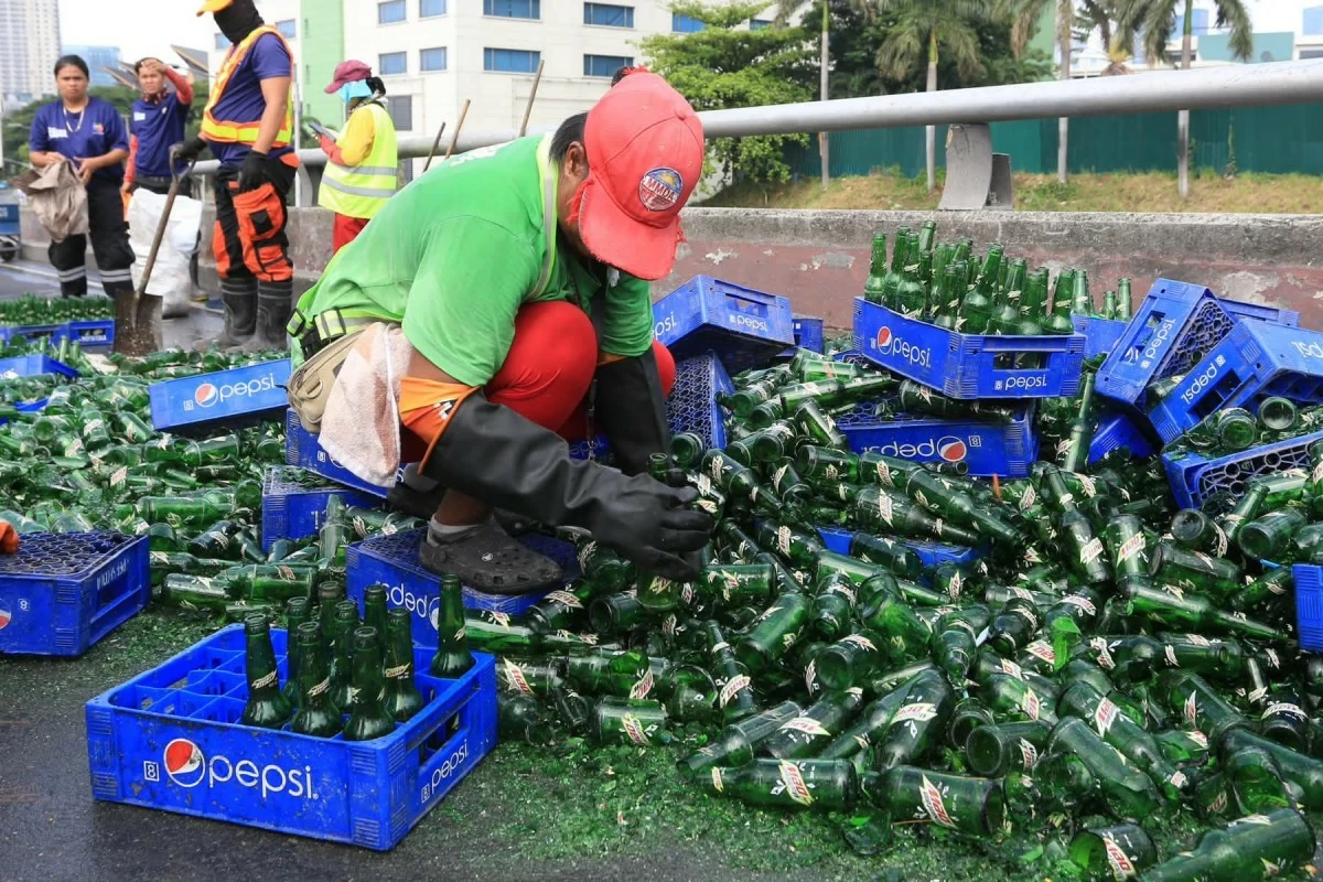 Personnel of the Metropolitan Manila Development Authority (MMDA) clear broken glass and soft drink bottles scattered along the southbound lane of the C-5 Ortigas Flyover in Pasig City on Sunday, June 14, 2026, following a collision involving two trailer trucks that left one person dead. (Photos by Santi San Juan)