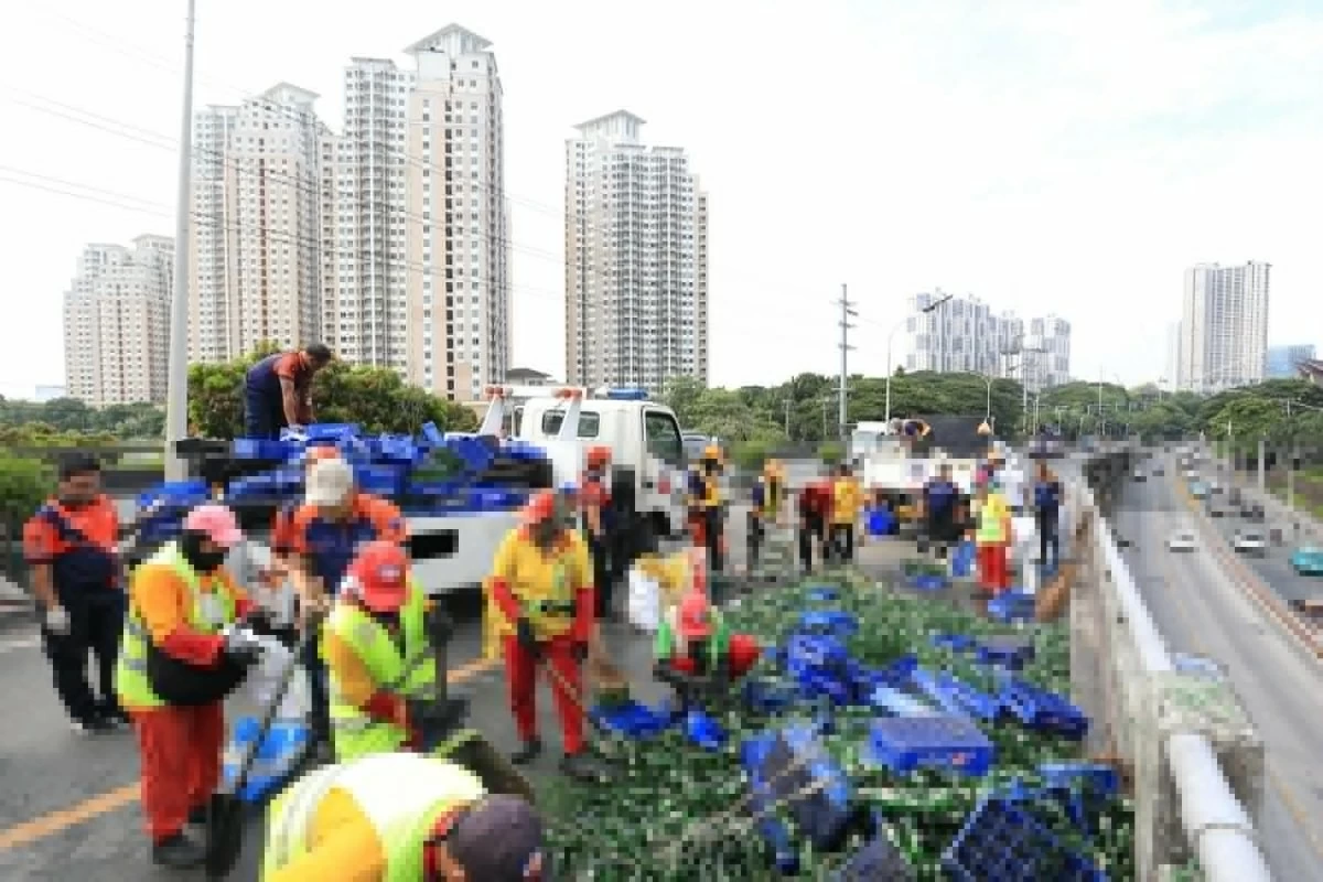 Personnel of the Metropolitan Manila Development Authority (MMDA) clear broken glass and soft drink bottles scattered along the southbound lane of the C-5 Ortigas Flyover in Pasig City on Sunday, June 14, 2026, following a collision involving two trailer trucks that left one person dead. (Photos by Santi San Juan)