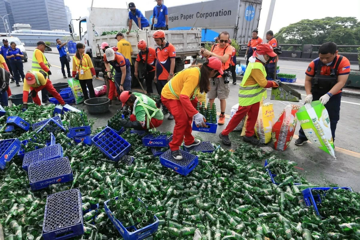 Personnel of the Metropolitan Manila Development Authority (MMDA) clear broken glass and soft drink bottles scattered along the southbound lane of the C-5 Ortigas Flyover in Pasig City on Sunday, June 14, 2026, following a collision involving two trailer trucks that left one person dead. (Photos by Santi San Juan)