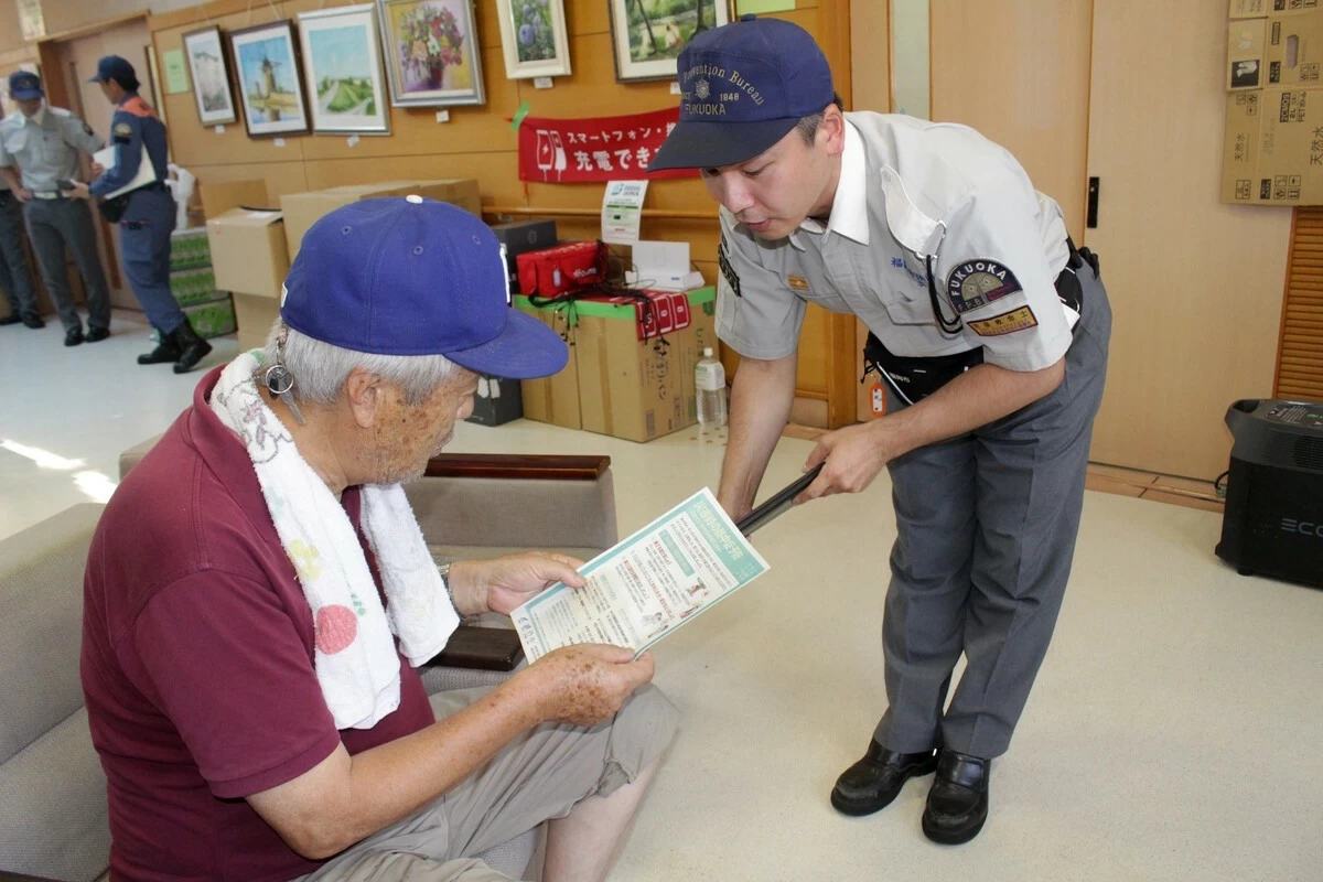 An emergency response team member, right, urges a man displaced by Tuesday's earthquake in Kumamoto Prefecture to take precautions against heatstroke in Yatsushiro, Kumamoto, on Sunday, August 2.