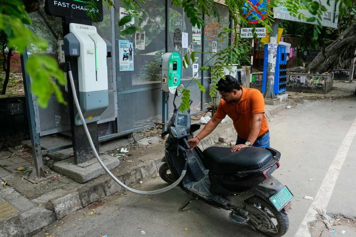 A person charges his electric scooter at a roadside charging station in New Delhi, India, Monday, July 13, 2026. (AP Photo/Manish Swarup)