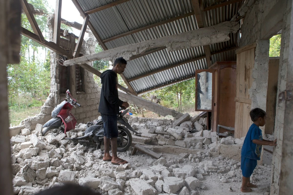 Saverinus Serli, left, inspects his earthquake-damaged house in Lelak, East Nusa Tenggara province, Indonesia, Sunday, Aug. 16, 2026. (AP Photo/Firdia Lisnawati)