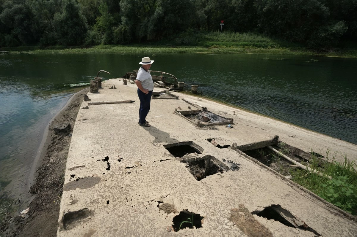 Stanislav Kozenko stands on the wreckage of an old steam boat, known as the Slovenian, as it is visible due to the low level of the Sava river near the town of Sremska Mitrovica, northwest of the capital Belgrade, Serbia, Tuesday, Aug. 18, 2026. (AP Photo/Darko Vojinovic)