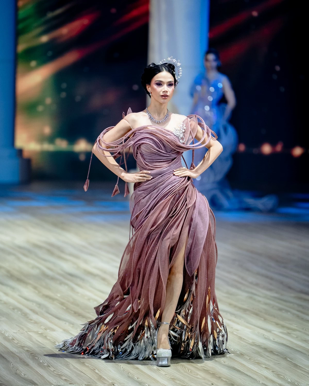 A structured drop-waist gown with asymmetrical drapes, cascading lines, adorned with metallic feather fringe, and silver cosmic accents.