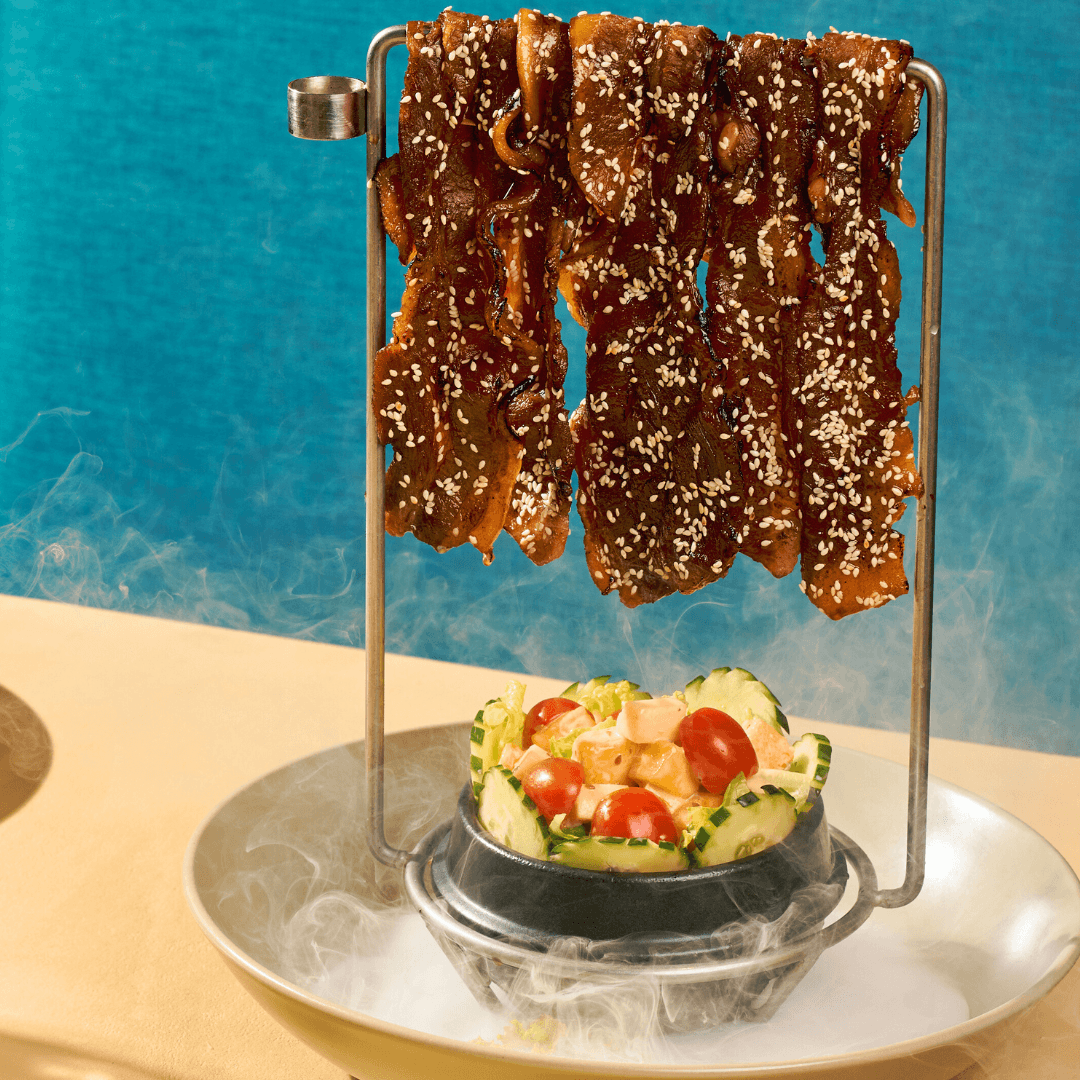 PORK BAKKWA SALAD Thin strips of seasoned pork hung over a rack, with a salad below.png