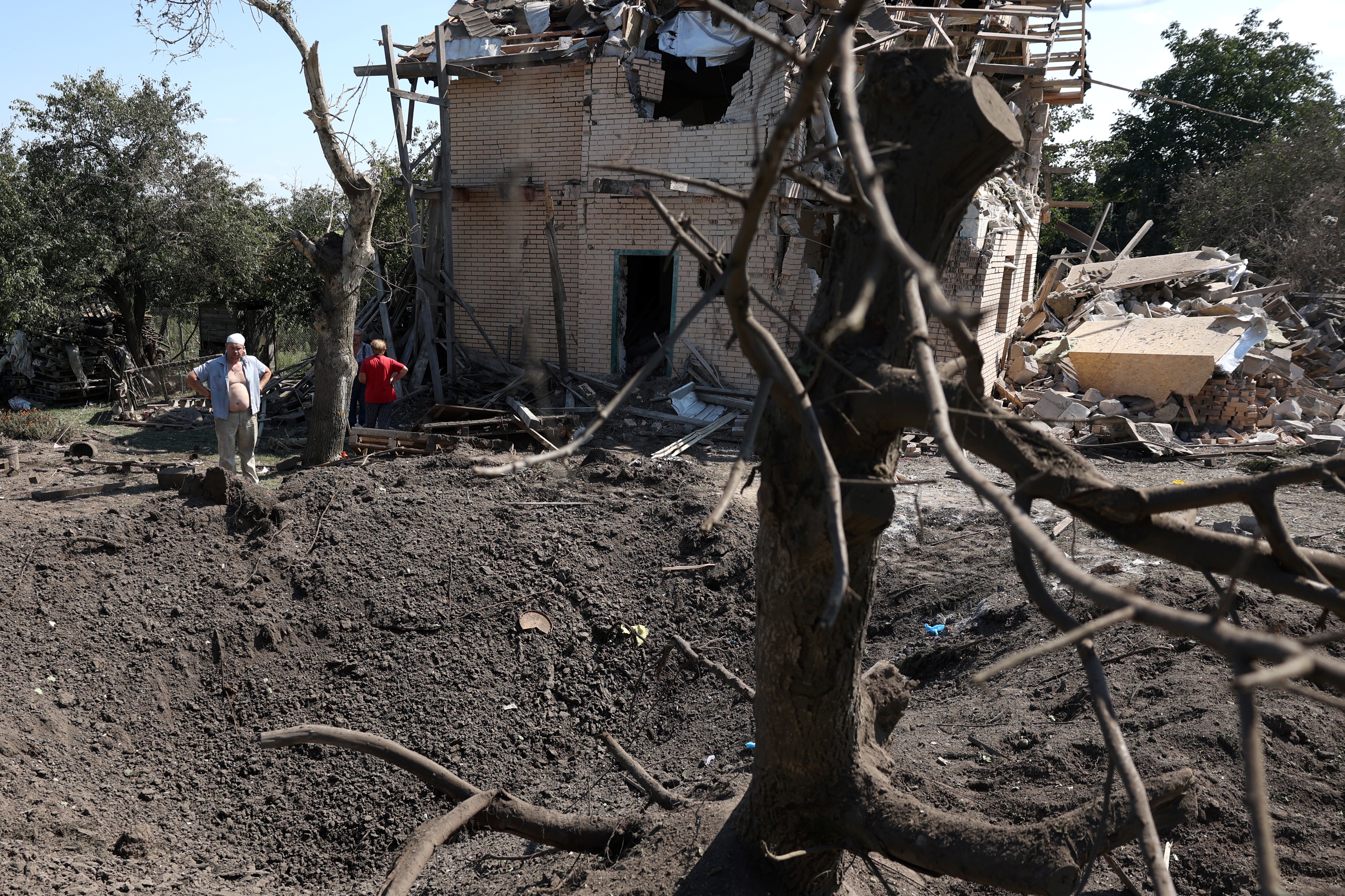 Local residents stand next to a crater and a destroyed residential house following a missile strike in Kyiv region, on August 27, 2023, amid the Russian invasion of Ukraine. (Photo by Anatolii STEPANOV / AFP)